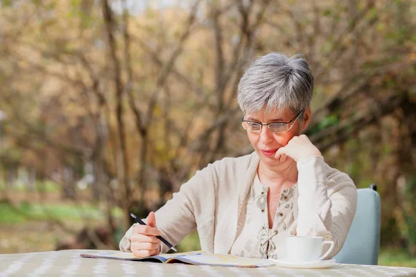 Starší žena v parku a řeší sudoku — Stock fotografie