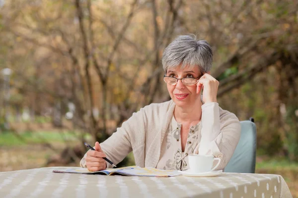 Mulher mais velha no parque e resolve sudoku — Fotografia de Stock