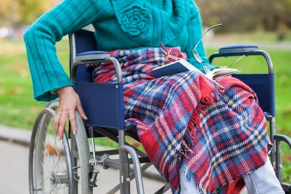 Літня жінка в інвалідному візку читає книгу — стокове фото