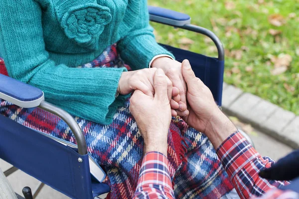 Мужские руки, держащие за руки женщину, которая сидит в инвалидном кресле — стоковое фото
