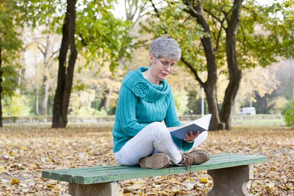 Middle aged woman in the park reading a book — Stock Photo, Image