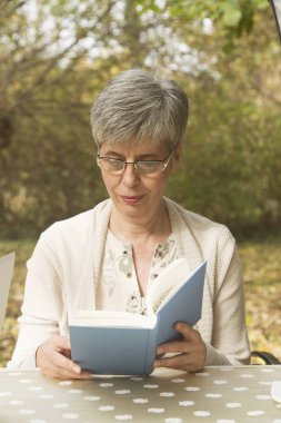Parkta kitap okuyan yaşlı bir kadın.