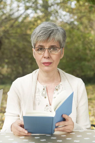 Äldre kvinna i parken läser en bok — Stockfoto