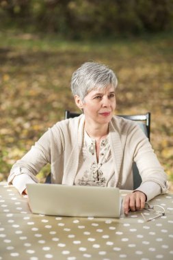 Bir bilgisayar ile bir parkta yaşlı kadın 