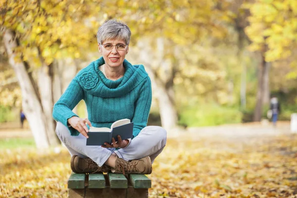 Femme plus âgée dans le parc lire un livre — Photo