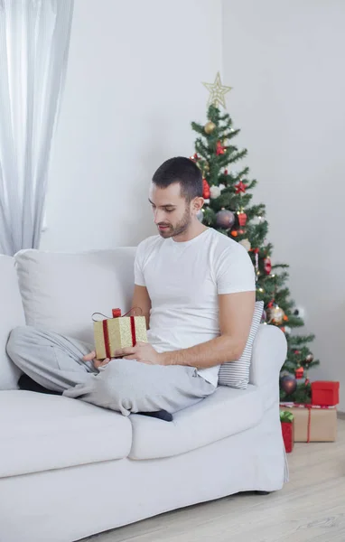 Homme sur le canapé tenant un cadeau de Noël — Photo