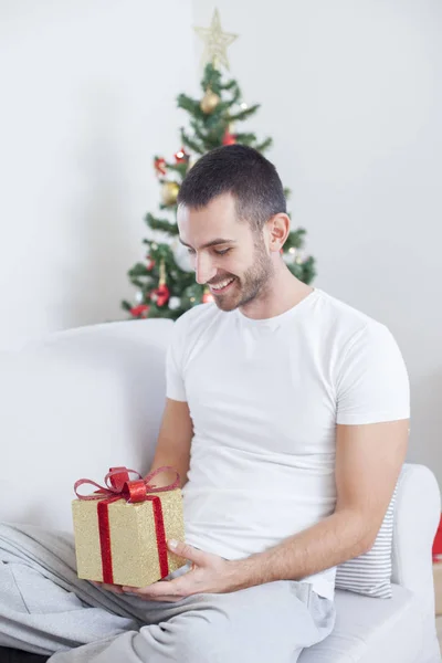 Om pe canapea ţinând un cadou de Crăciun — Fotografie, imagine de stoc