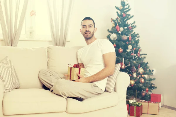 Homme sur le canapé tenant un cadeau de Noël — Photo