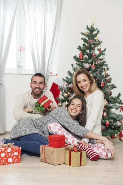 Friends sitting next to Christmas tree with presents — Stock Photo, Image