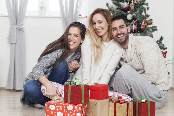 Amigos sentados ao lado da árvore de Natal com presentes — Fotografia de Stock