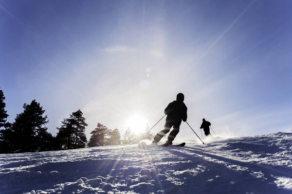 Skiing, silhouette of skiers on the ski slope with the sun's rays on a blue sky