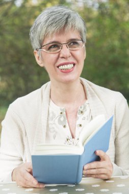 Parkta kitap okuyan yaşlı bir kadın.