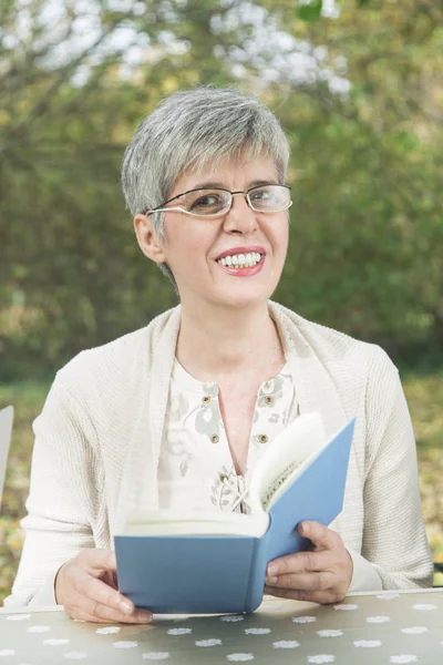 Parkta kitap okuyan yaşlı bir kadın.