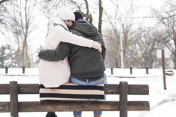 Пара, сидящая на скамейке в снежном парке — стоковое фото