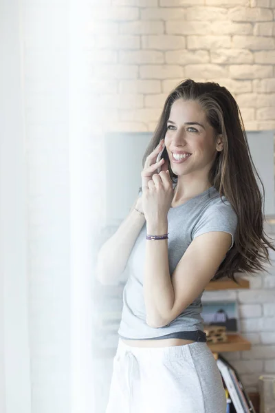 Mulher usando celular ao lado da janela — Fotografia de Stock