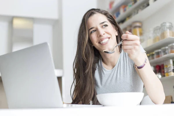 Mujer desayunando sano cerca de la computadora portátil — Foto de Stock