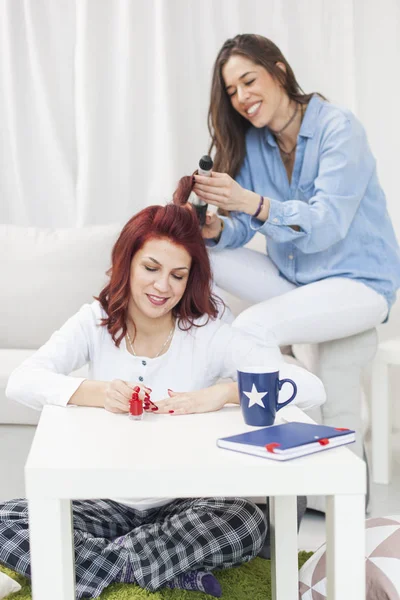 Menina curling cabelo do amigo com rolos em uma cama na sala de estar — Fotografia de Stock