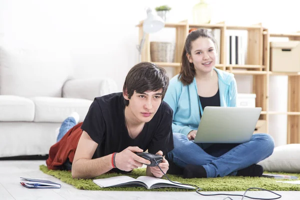 Dois amigos adolescentes. Menino jogando console de jogos, menina trabalhando em la — Fotografia de Stock