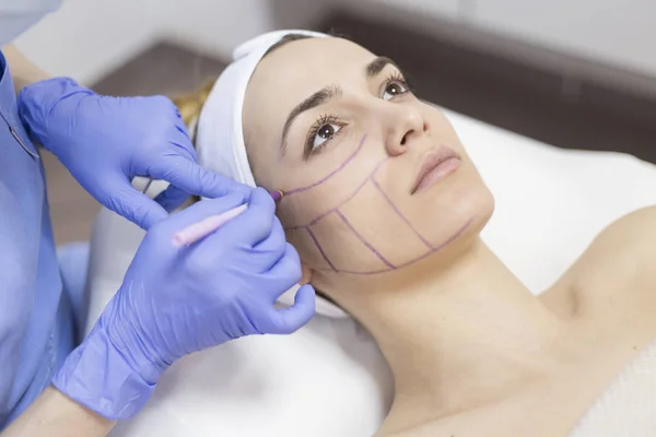 Beautician draw correction lines on woman face