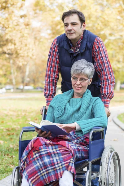 Жінка в інвалідному візку з сином, що йде серед парку — стокове фото