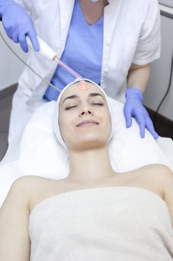 Woman getting facial laser treatment clipart