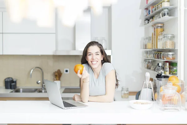 Женщина держит оранжевый перед ноутбуком — стоковое фото