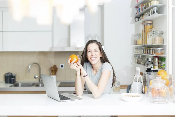 Kobieta trzyma orange przed laptop — Zdjęcie stockowe