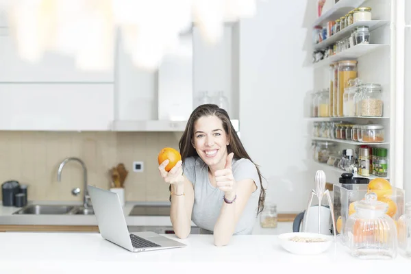 Женщина держит оранжевый перед ноутбуком — стоковое фото
