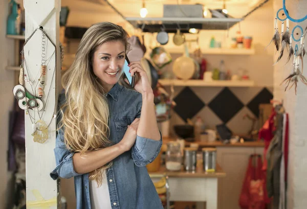 Schöne junge Frau in einer Hipster-Küche SMS auf ihrem Handy in Jeans und weißem Hemd — Stockfoto