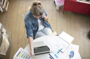 Genç ve güzel bir kadın, beyaz bir masada dizüstü bilgisayarı olan bir evden bilgisayar için çalışıyor.