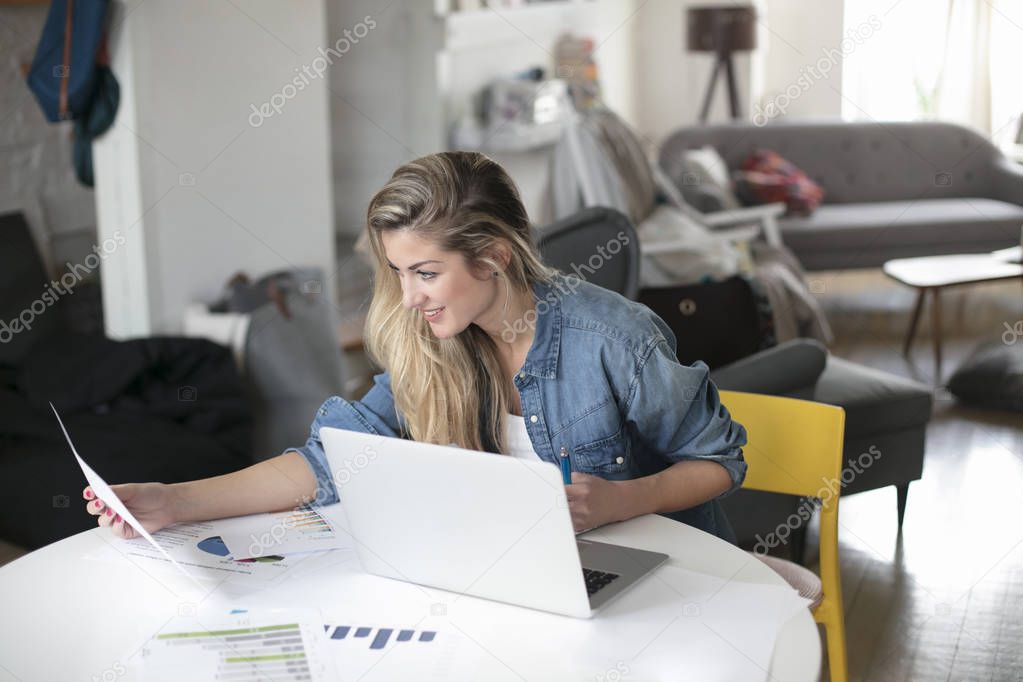 Young beautiful woman works for a computer from a home with a laptop on a white desk as a freelancer