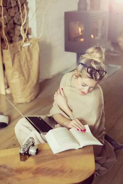 リビング ルームで若い美しい女性の床に座って 暖炉の奥に冷たいのための毛布で覆われて コンピューターを介して友人と通信 — ストック写真
