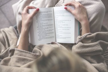 Genç güzel kadın oturur ve bir battaniye ile örtülü bir teras üzerine bir kitap okur ve arka planda bir şömine var