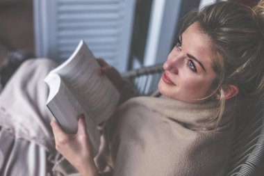 Genç güzel kadın oturur ve bir battaniye ile örtülü bir teras üzerine bir kitap okur 