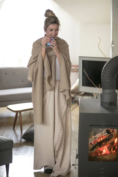 Beautiful middle-aged woman drinks tea from a glass in a cold living room dressed in a cotton becouse of cold winter. A sick girl drinks from a blue cup in the living room.