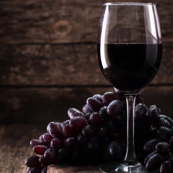 Glass of red wine, served with grapes on a wooden background — Stock Photo, Image