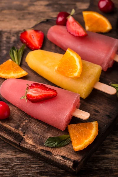 Uppfriskande frukt popsicle klubbor på träbord med bär och frukter — Stockfoto