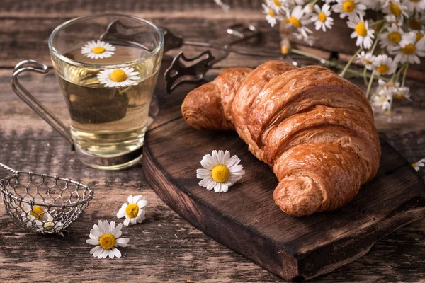 Frukost med örtte och croissant på vintage träbord — Stockfoto