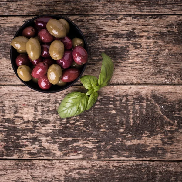 Olives on wooden dark table with basil — Stock Photo, Image