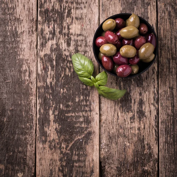 Olives on wooden dark table with basil — Stock Photo, Image