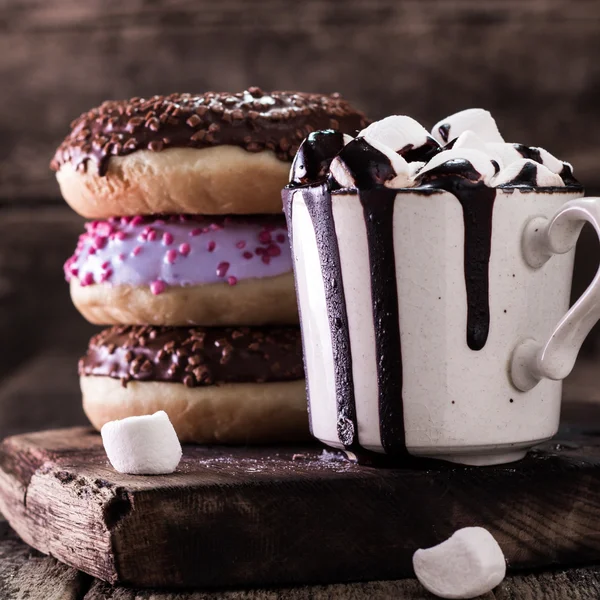 Donuts e uma xícara de café com chocolate em uma mesa de madeira — Fotografia de Stock