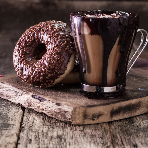 Donuts e uma xícara de café com chocolate em uma mesa de madeira — Fotografia de Stock