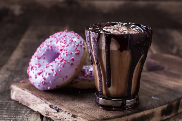 Donuts e uma xícara de café com chocolate em uma mesa de madeira — Fotografia de Stock