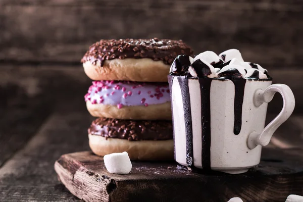 Donuts und eine Tasse Kaffee mit Schokolade auf einem Holztisch — Stockfoto