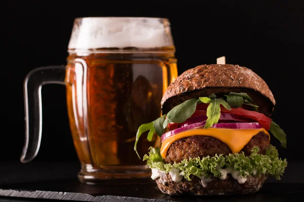 Hamburguesa fresca y sabrosa con una cerveza en una mesa de madera . — Foto de Stock