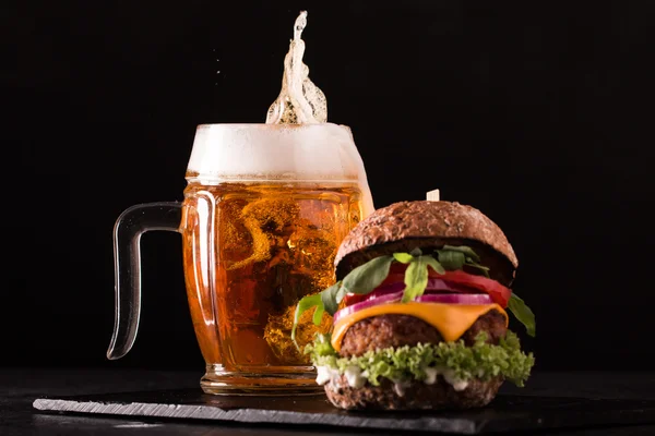 Hamburguesa fresca y sabrosa con una cerveza en una mesa de madera . — Foto de Stock