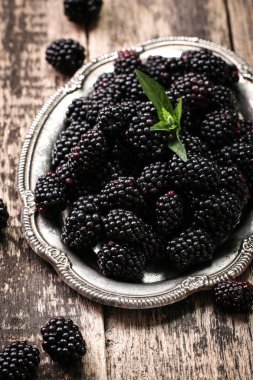 Ahşap arka plan üzerinde çuval bezi kumaş üzerine seramik bir kasede olgun böğürtlen kapatın. Rustik tarzı, seçici odak