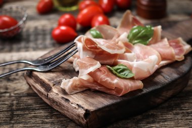 Fesleğenli domates ahşap kesme tahtası, antika arka plan üzerinde ince dilim jambon ile karışık