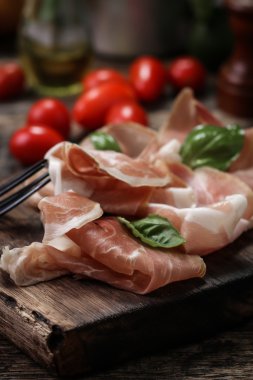Fesleğenli domates ahşap kesme tahtası, antika arka plan üzerinde ince dilim jambon ile karışık