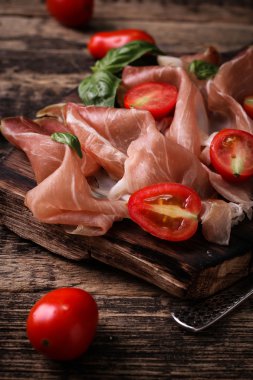 Fesleğenli domates ahşap kesme tahtası, antika arka plan üzerinde ince dilim jambon ile karışık